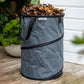 Charcoal colored Pop up Waste Bag full of brown leaves sitting on a wooden deck