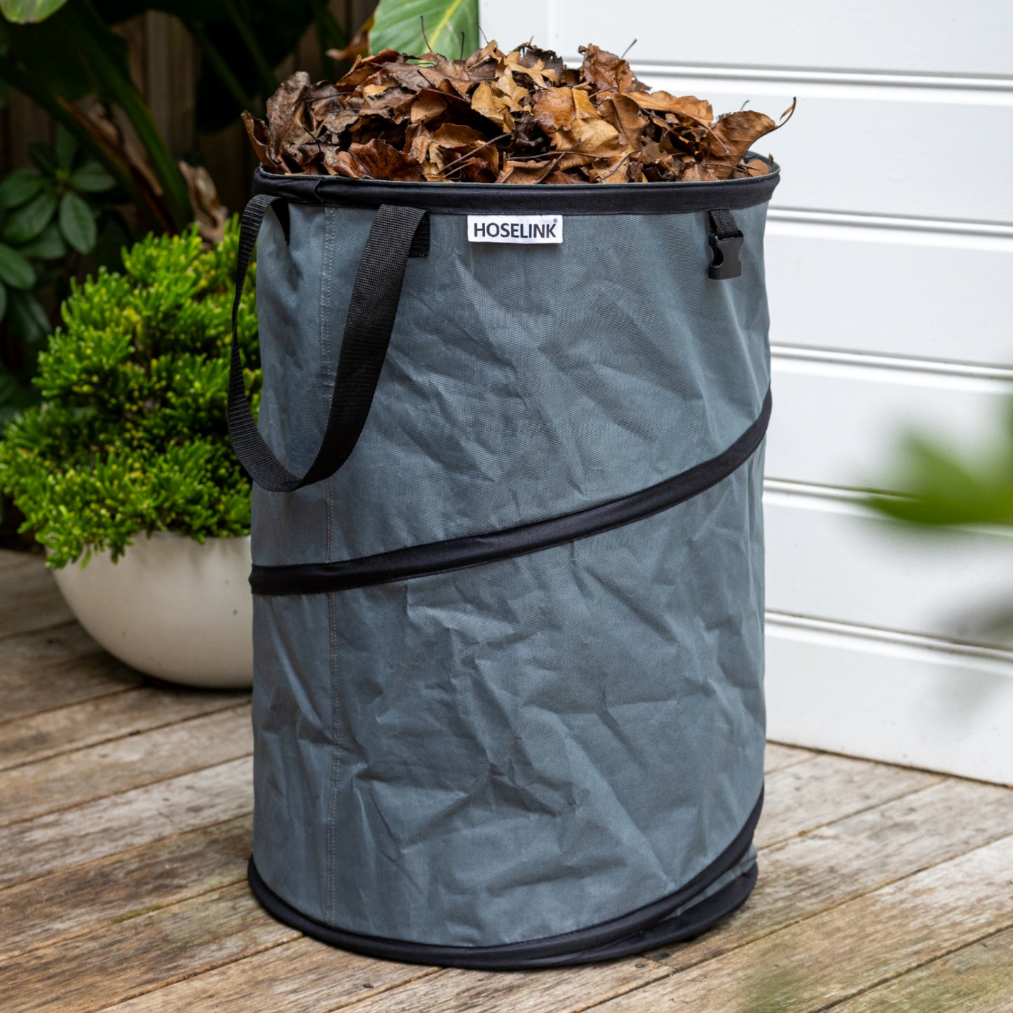 Charcoal colored Pop up Waste Bag full of brown leaves sitting on a wooden deck