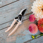 peach secateurs on a table with pink flowers next to them