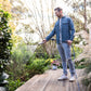 person standing on deck watering green bushes with the brass garden hose nozzle with trees in the background